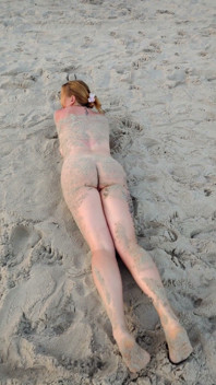 En primer plano. Usted mira como una modelo tetona, de su presencia, se desnuda en la playa, se baña, y juega en la arena.