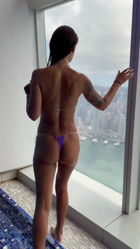 Monika Fox in Purple Bikini Swims in Pool & Poses by Window Against Background of City